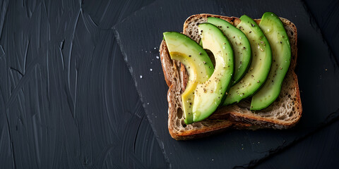 A black wooden table with a blackboard surface and a sandwich with sliced avocado on top.