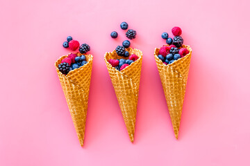 Fresh berries in waffle cones on pink background top view