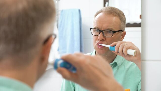 Middle-aged man brushing teeth with a electric brush in bathroom