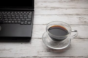 ガラス製のコーヒーカップとノートパソコン