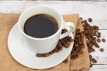 白い木目テーブルの上に置かれたコーヒーカップとコーヒー豆