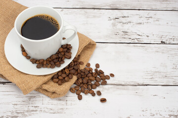 白い木目テーブルの上に置かれたコーヒーカップとコーヒー豆