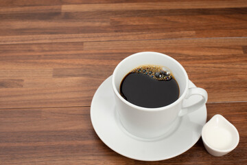木目テーブルの上に置かれたコーヒーカップとコーヒーフレッシュ