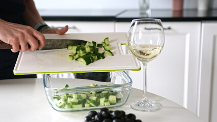 Girl Pours Chopped Cucumbers Into Bowl For Greek Salad At Home In Bright Kitchen