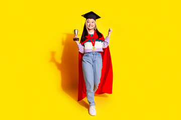 Full length photo of ecstatic girl dressed striped shirt hold goblet raising fist up win competition isolated on yellow color background