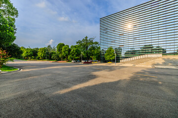 Asphalt road and green forest with glass wall building background in city park