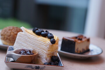 A piece of blueberry crepe cake topped with blueberry on the plate with blur of espresso macadamia cheese cake and choux cream.