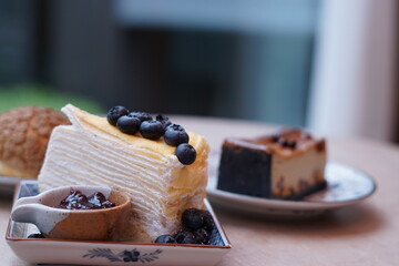 A piece of blueberry crepe cake topped with blueberry on the plate with blur of espresso macadamia cheese cake and choux cream.