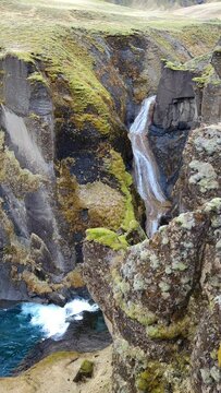 A serene blue cascade flows amidst dark rocks adorned with lush green moss.
