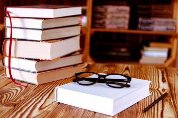 White book and black reading glasses on the background of bookshelves