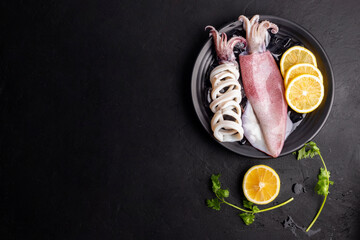 Fresh raw squid. Raw squid on a black plate with ice. Lemon slices. Top view and copy space for...