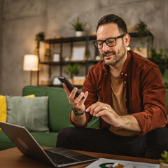 Adult man work from home on laptop and use mobile phone for message