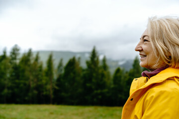 Close up portrait Smiling Caucasian Senior woman in yellow rain jacket in Misty autumn mountain...
