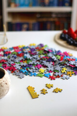 Colorful jigsaw puzzle pieces, cup of tea or coffee, eyeglasses and fresh berries for snacking. Hygge at home. Selective focus.