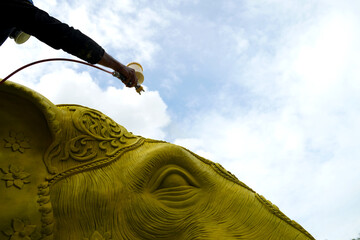 An artist spray paints an elephant statue with gold paint.