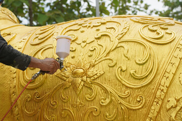 An artist spray paints an elephant statue with gold paint.
