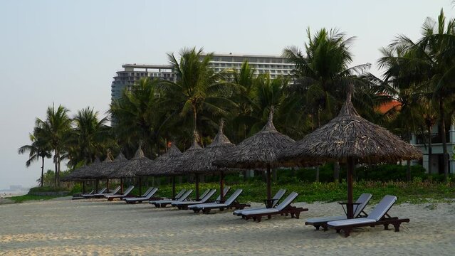 Beautiful view of the hotel grounds with a sandy beach, umbrellas made of palm leaves and sun loungers along the seashore