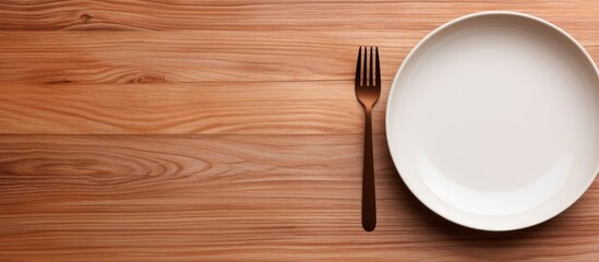 Top view of a white ceramic dish with a stainless fork and spoon placed on a wooden mat textured background on a dining table creating the perfect copy space image