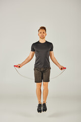 A young sportsman in active wear is energetically jumping with a skipping rope in front of a white background.