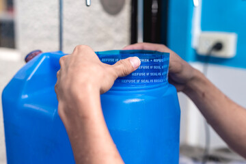 Placing a plastic seal on the lid of a blue 20 liter HPDE water container. A purified water...