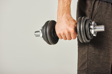 A young sportsman in active wear grips a pair of dumbbells in a studio with a grey background,...