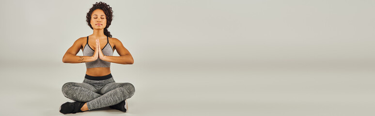Young African American woman in activewear gracefully practicing yoga on a serene gray background...