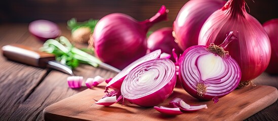 A female hand is seen meticulously slicing big shallots red onions on a wooden cutting board with a knife The copy space image has a close up view