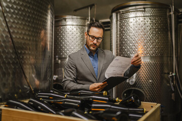 Adult man stand sommelier in basement look wine and hold clipboard