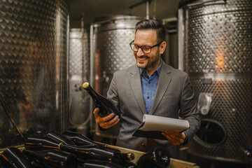 Adult man stand sommelier in basement hold bottle wine and clipboard