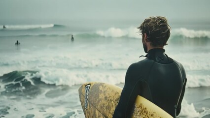 A man wearing a wet suit holding a yellow surfboard.