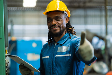 A man in a blue work uniform is holding a tablet and giving a thumbs up. He is wearing a yellow...