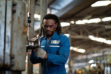 A man in a blue jumpsuit is working on a machine. He is wearing gloves and he is focused on his task