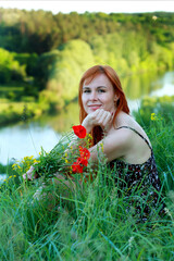 A girl with wild poppies enjoys the view from a hill near the river. Joy, happiness, serenity. Wild poppies by the river.