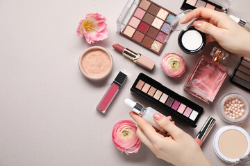 Fototapeta premium Woman with different makeup products and beautiful spring flowers on grey background, top view. Space for text