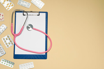 Stethoscope, clipboard and pills on beige background, flat lay. Space for text