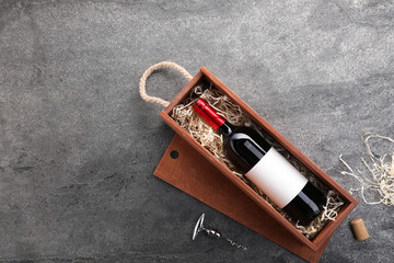 Bottle of wine in wooden box and corkscrew on dark textured table, flat lay. Space for text