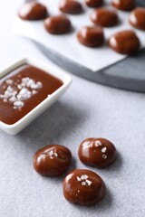 Tasty candies, caramel sauce and salt on light grey table