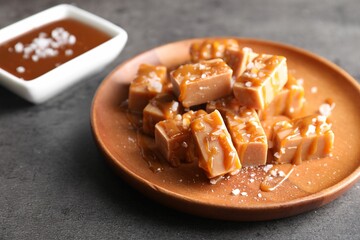 Plate with tasty candies, caramel sauce and salt on grey table, closeup