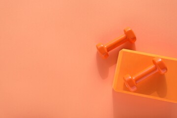 Dumbbells and yoga block on coral background, flat lay. Space for text