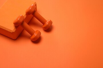 Dumbbells and yoga block on orange background. Space for text