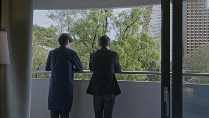 Fototapeta premium Rear view of two businessmen standing on the balcony and communicating. Stock clip. Men in hotel room at informal meeting.