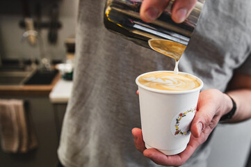 Close-up of a person pouring milk into a coffee cup, creating latte art, with a blurred kitchen...