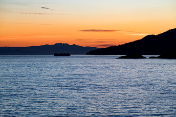 ferry , ship or boat rounding Bowen island on the Salish Sea with Vancouver Island in the distance at sunset, dusk, or twilight