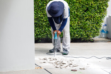 Builder worker with pneumatic hammer drill equipment breaking concrete at floor
