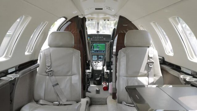 Modern cabin of private plane exuding luxury featuring plush leather seats and elegant wood paneling. Control panel in front with various switches, buttons and indicators