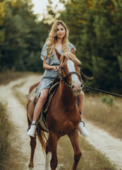 Fototapeta premium A young beautiful woman rides a horse in the forest in autumn. Horseback riding in the evening in autumn.