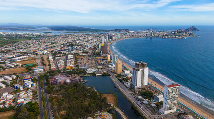 An aerial view of Mazatlán Beach on a sunny morning, showcasing the blue ocean's gentle waves meeting the sandy shores of this popular tourist destination