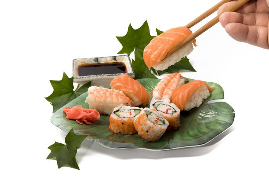 chopsticks holding a piece of salmon sahimi from a plate of sushi isolated on white