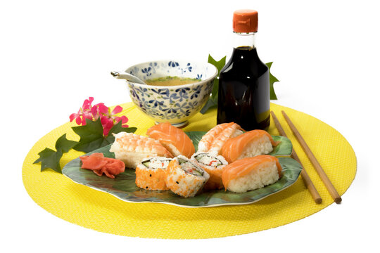 Asian lunch of salmon and shrimp sahimi and a sushi roll and soy sauce on a yellow place mat isolated on white
