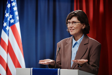 Mature female deputy or minister opening her palms and looking at electorate while explaining steps...